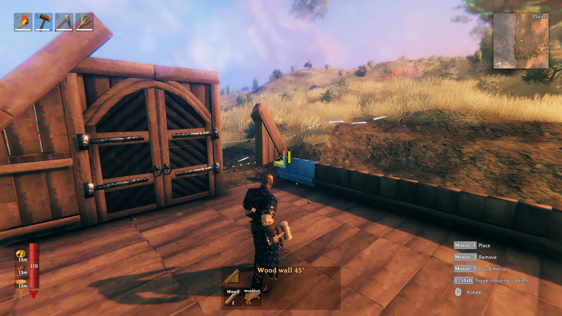 A Valheim character holding a hammer beside a partly built wooden house overlooking the Plains.
