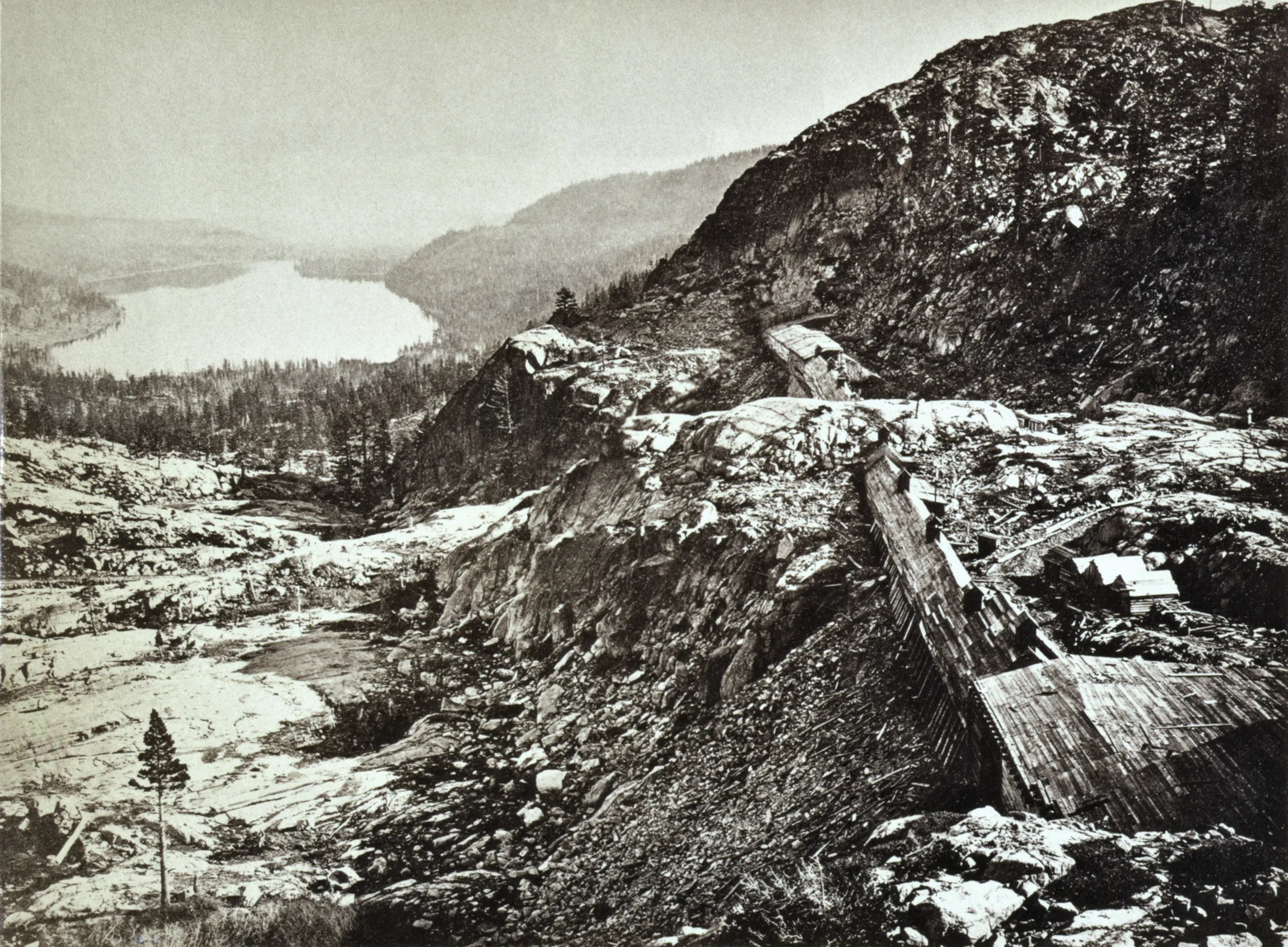 Historic photograph looking past railroad snow sheds across rocky Sierra Nevada slopes toward Donner Lake.
