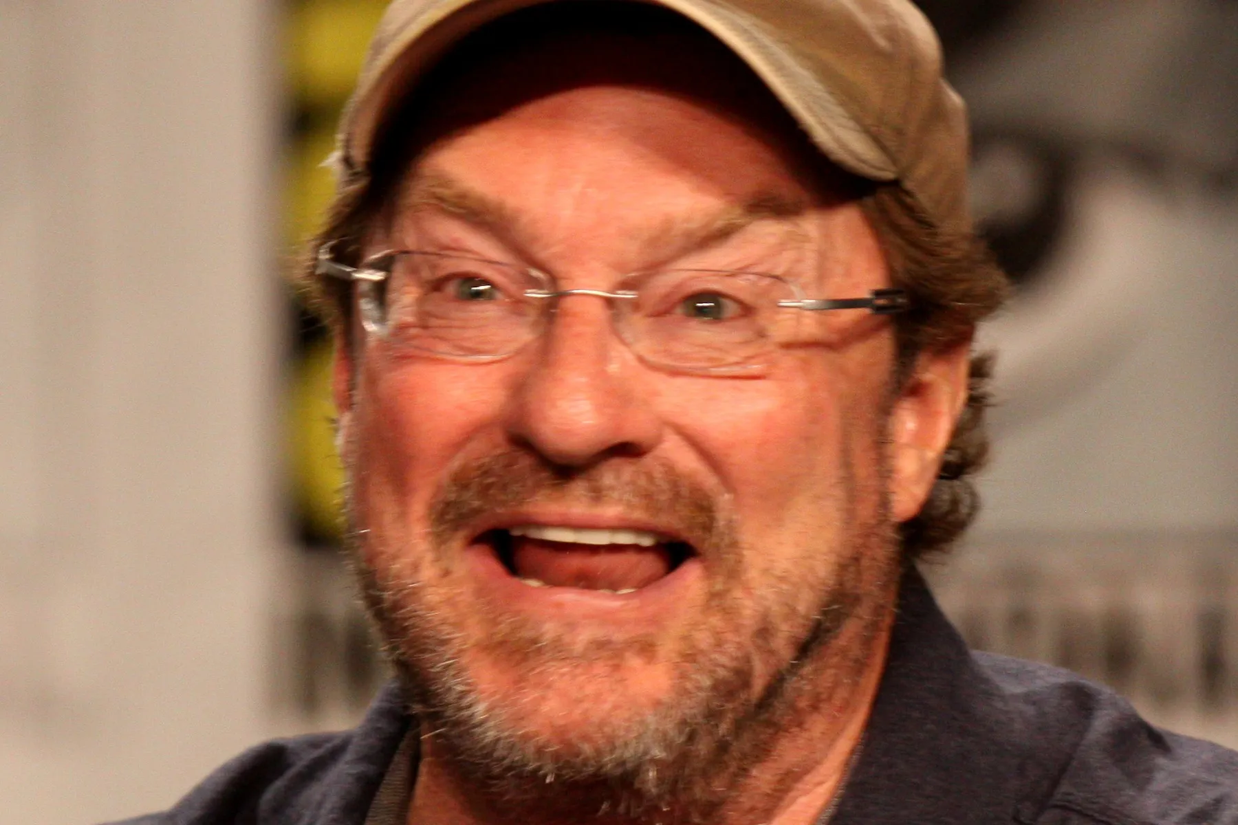 Stephen Root smiling, wearing glasses and a cap.